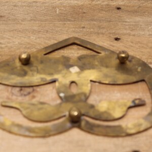 May include: A brass trivet with a decorative design of two birds. The trivet has four round knobs on the top and bottom.