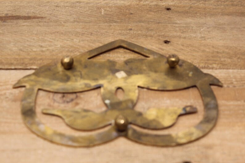 May include: A brass trivet with a decorative design of two birds. The trivet has four round knobs on the top and bottom.