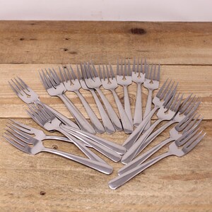 May include: A selection of stainless steel forks displayed on a wooden surface. Each fork features four tines and a streamlined handle. The forks are arranged, suggesting a dining set for use at a table.