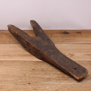 May include: A vintage, dark brown wooden boot jack. The tool has a Y-shaped top and a long, flat handle. The antique item shows signs of wear and age, with a small hole at the end of the handle.