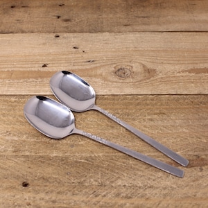 May include: Two silver spoons with ornate handles on a wooden surface.