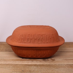 May include: A terracotta oval baking dish with a lid. The lid has the words "Schlemmertopf" embossed on it.