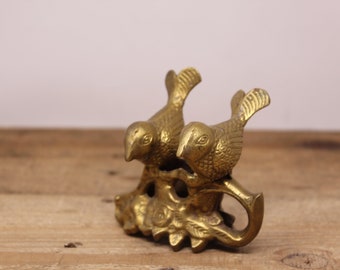 May include: A gold-toned metal bird figurine with two birds perched on a leafy branch. The birds are facing each other and have detailed features.
