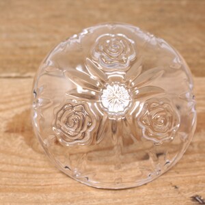 May include: A clear glass bowl with a raised design of three roses. The bowl is on a wooden surface.