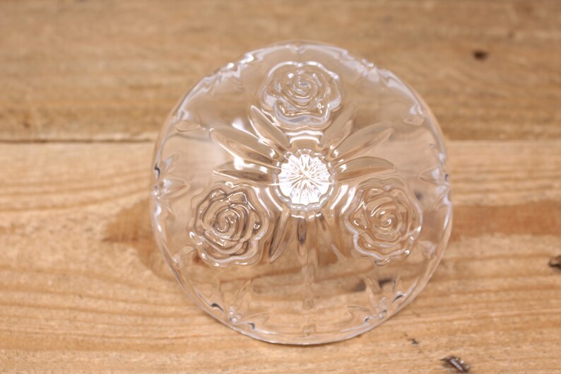 May include: A clear glass bowl with a raised design of three roses. The bowl is on a wooden surface.