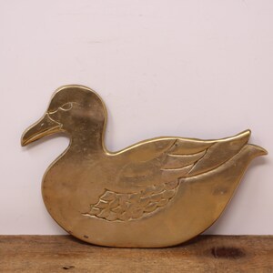 Pode incluir: Um descanso de panela de metal dourado em forma de pato. O pato tem um design detalhado com penas e uma asa.