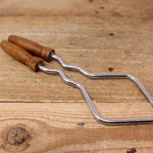 May include: A silver metal saw frame with two wooden handles. The frame is bent into a square shape.