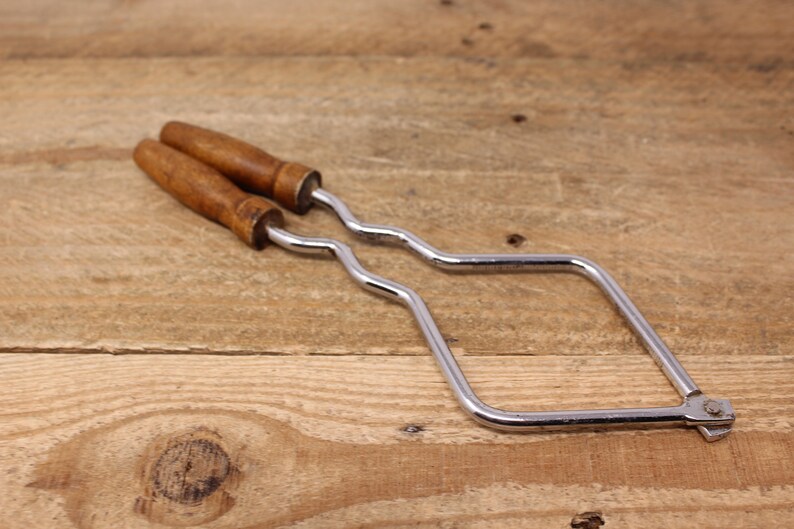 May include: A silver metal saw frame with two wooden handles. The frame is bent into a square shape.