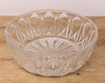 May include: A clear glass bowl with a decorative, cut-glass design. The bowl has a wide, round shape and a scalloped rim.
