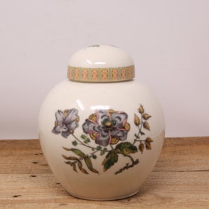 May include: A white ceramic jar with a floral design. The jar has a lid with a gold and orange trim. The flowers are pink, purple, and green.