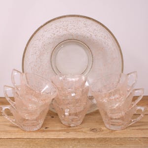 May include: A vintage glass punch bowl and cups set with a pink swirl design. The bowl has a clear glass base and a pink swirl design throughout. The cups are also clear glass with a pink swirl design. The set is perfect for entertaining.