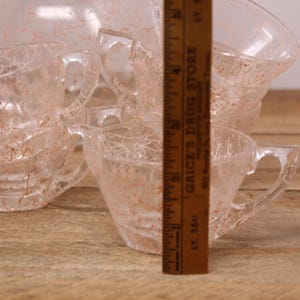 May include: Set of six clear glass teacups with a delicate, crackled pattern. The cups have a light pink hue and are stacked on top of each other.