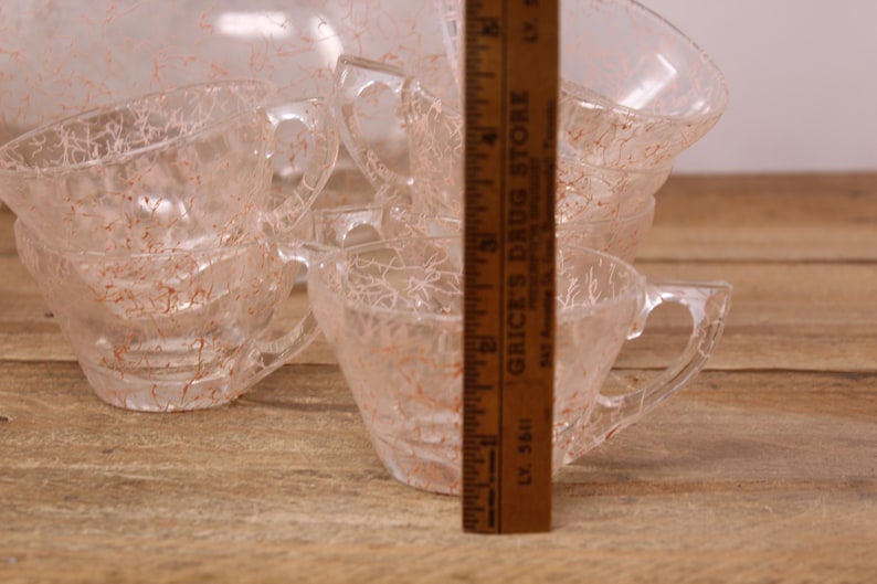 May include: Set of six clear glass teacups with a delicate, crackled pattern. The cups have a light pink hue and are stacked on top of each other.