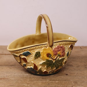 May include: A yellow ceramic basket with a brown handle and floral design. The basket is decorated with yellow, pink, and green flowers and leaves.