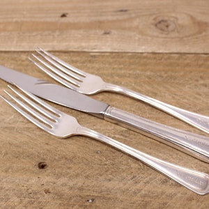 May include: Three silver-plated pieces of cutlery, a knife and two forks, on a wooden surface. The knife and forks have the word "Wallace" engraved on the handles.