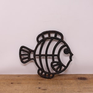 May include: Black cast iron fish-shaped trivet. The trivet has a detailed design with a striped pattern and a large eye.