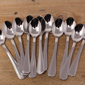 May include: A set of twelve silver teaspoons arranged in a fan shape on a wooden surface.