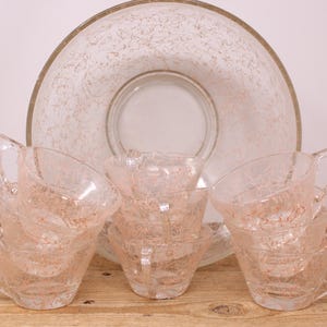 May include: A set of six pink glass cups and a matching bowl with a frosted, speckled design. The cups have handles and are stacked in pairs.