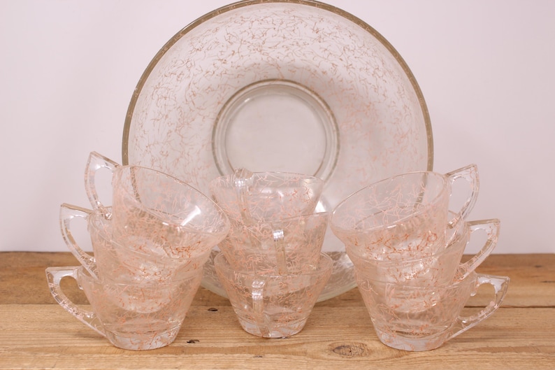 May include: A set of six pink glass cups and a matching bowl with a frosted, speckled design. The cups have handles and are stacked in pairs.