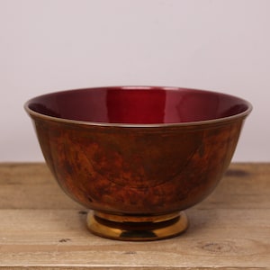 May include: A red and gold ceramic bowl with a wide rim and a footed base. The bowl has a glossy finish and a slightly distressed look.