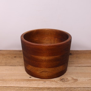 May include: A round wooden bowl with a dark brown finish. The bowl is made of natural wood and has a smooth, polished surface.