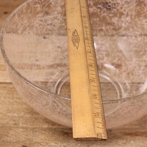 May include: A clear glass bowl with a white crackle pattern. The bowl is sitting on a wooden surface with a ruler next to it.