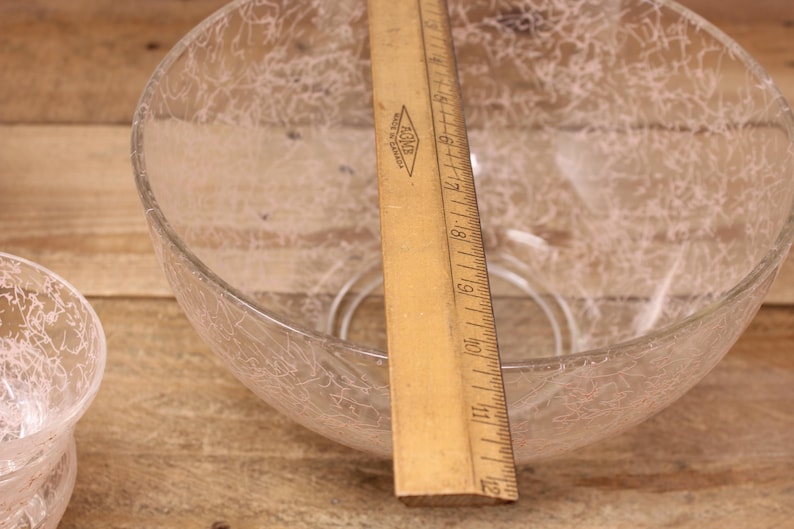 May include: A clear glass bowl with a white crackle pattern. The bowl is sitting on a wooden surface with a ruler next to it.