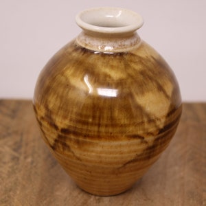 May include: A small, round, brown and white ceramic vase with a glossy finish. The vase has a wide mouth and a narrow neck.