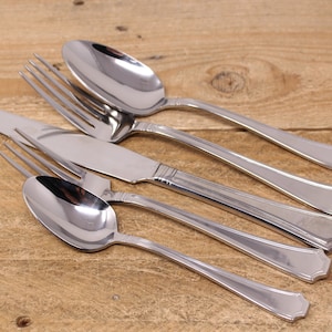 May include: A set of four silver-toned cutlery pieces, including a fork, knife, and two spoons, arranged on a wooden surface.