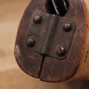 May include: Close-up of a wooden shoe stretcher with a metal clamp and screws. The stretcher has a brown finish and is made of wood. The clamp is made of metal and has a black finish.