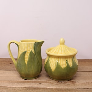 Peut inclure: Un ensemble de pot à crème et de sucrier en céramique jaune et verte en forme d'épis de maïs. Le pot à crème a une poignée et le sucrier a un couvercle.