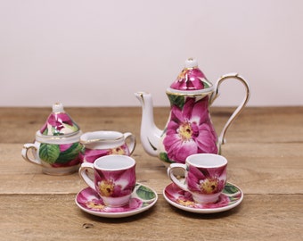 May include: A floral tea set with a teapot, creamer, sugar bowl, and two teacups and saucers. The set is decorated with pink and green floral designs.