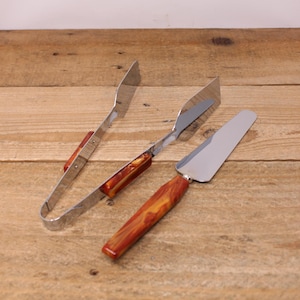 May include: A set of two kitchen utensils with brown and orange marbled handles. The utensils are a silver spatula and a pair of silver tongs.