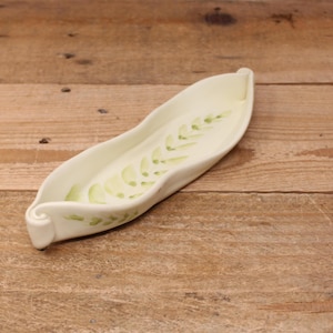 May include: Cream-coloured ceramic serving dish with a light green leaf design. The dish is long and narrow with a curved shape and rolled edges. The leaf pattern is painted on the inside of the dish.