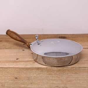 May include: A silver serving dish with a wooden handle. The dish has a decorative design on the top and a beaded edge.