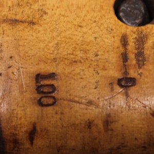 May include: Close-up of a wooden surface with the number "100" carved into it. The surface is a light brown color and has a few scratches.