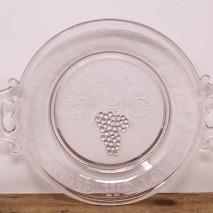 May include: A clear glass serving dish with two handles. The dish features a grapevine design with a bunch of grapes in the centre. The words "Wine Makes Me Happy" are etched around the rim.