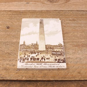 May include: A vintage postcard featuring a black and white image of the Bunker Hill Monument in Boston, Massachusetts. The text on the postcard reads "Bunker Hill Monument Dedicated June 17th 1843 Height 221 feet."