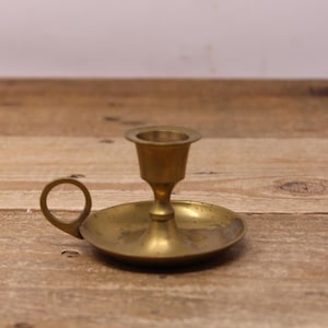 May include: A vintage brass candlestick holder with a circular handle and a small dish-shaped base. The candle holder is made of brass and has a warm, golden color. The design is simple and classic, suitable for various decor styles.