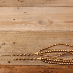 May include: A gold multi-strand necklace with round beads. The necklace is made of multiple strands of gold chain and gold beads.