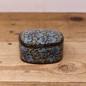 May include: A small, oval-shaped box with a blue and black floral design. The box is made of paper mache and has a glossy finish.