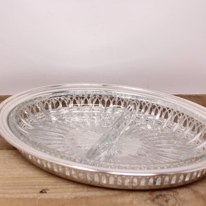 May include: A silver-plated serving dish with a clear glass insert divided into three sections. The dish has a decorative, scalloped edge.