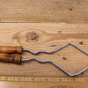May include: A pair of vintage metal and wood jig saw frames with a wavy blade. The frames are silver and the handles are brown wood. The frames are about 7 inches long.