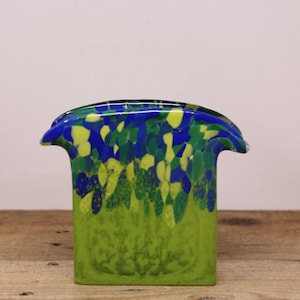 May include: A green glass napkin holder with blue and yellow swirls. The holder has a unique shape with two curved sides.