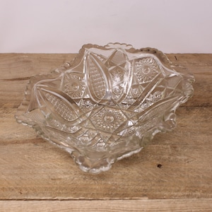 May include: A clear glass bowl with a scalloped edge and intricate cut glass design. The bowl is empty and sitting on a wooden surface.