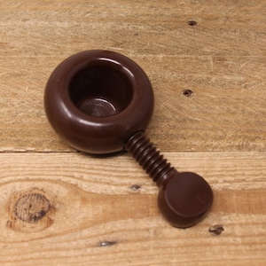 May include: A brown plastic nutcracker with a screw-like handle. The nutcracker has a round, bowl-shaped top with a small hole in the center.