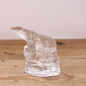 May include: A clear glass sculpture of a polar bear standing on a piece of ice. The sculpture is detailed and realistic, with the bear's fur and claws visible.