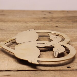 May include: A brass heart-shaped hot pad featuring two stylised geese intertwined. The geese are facing each other and their necks are curved to form the heart shape.