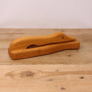Peut inclure: Un casse-noisette en bois en forme de canard avec une finition brune. La tête du canard est relevée et son bec est ouvert.
