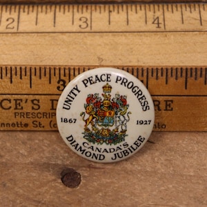 May include: A vintage white button with the text "UNITY PEACE PROGRESS" and "CANADA'S DIAMOND JUBILEE". The button features a detailed coat of arms with a crown, lion, and unicorn. Dates 1867 and 1927 are also visible.